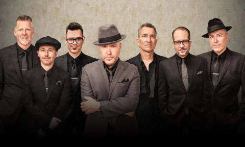 Bandmates from Big Bad Voodoo Daddy pose in front of a gray backdrop.